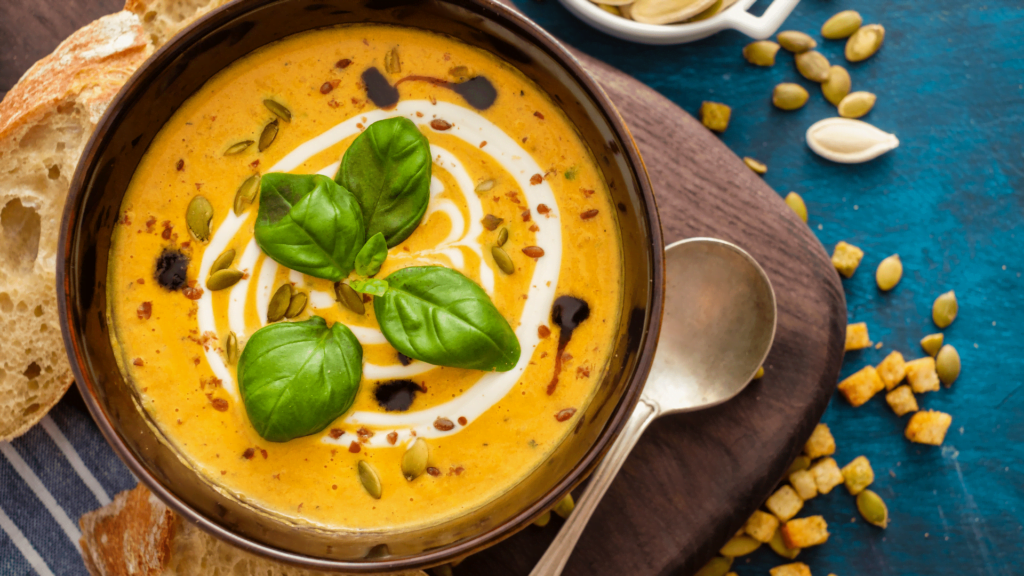 Velouté de potiron au foie gras dans un bol avec des noisettes concassées et une feuille de basilic avec de la crème.
