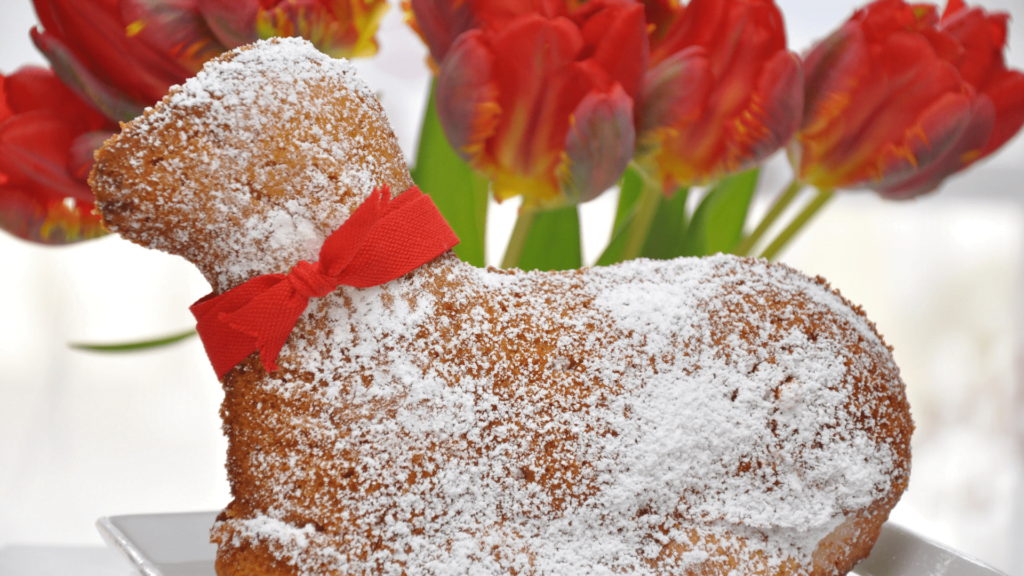 Gâteau en forme d'agneau saupoudré de sucre glace devant un bouquet de tulipes.